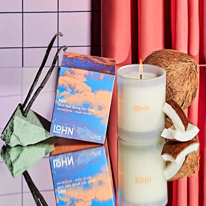 LOHN candle with packaging, vanilla bean, and coconut on a reflective surface with a colorful background.