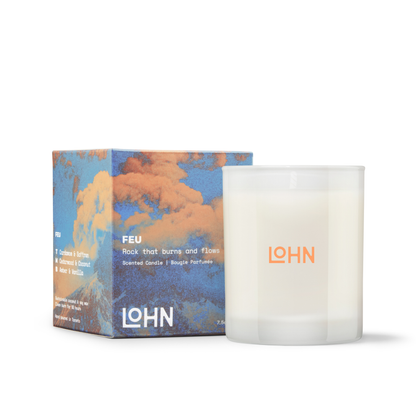 A frosted glass scented candle in a clear glass vessel next to its matching box, both featuring a blue and orange cloud design with the brand name LOHN.