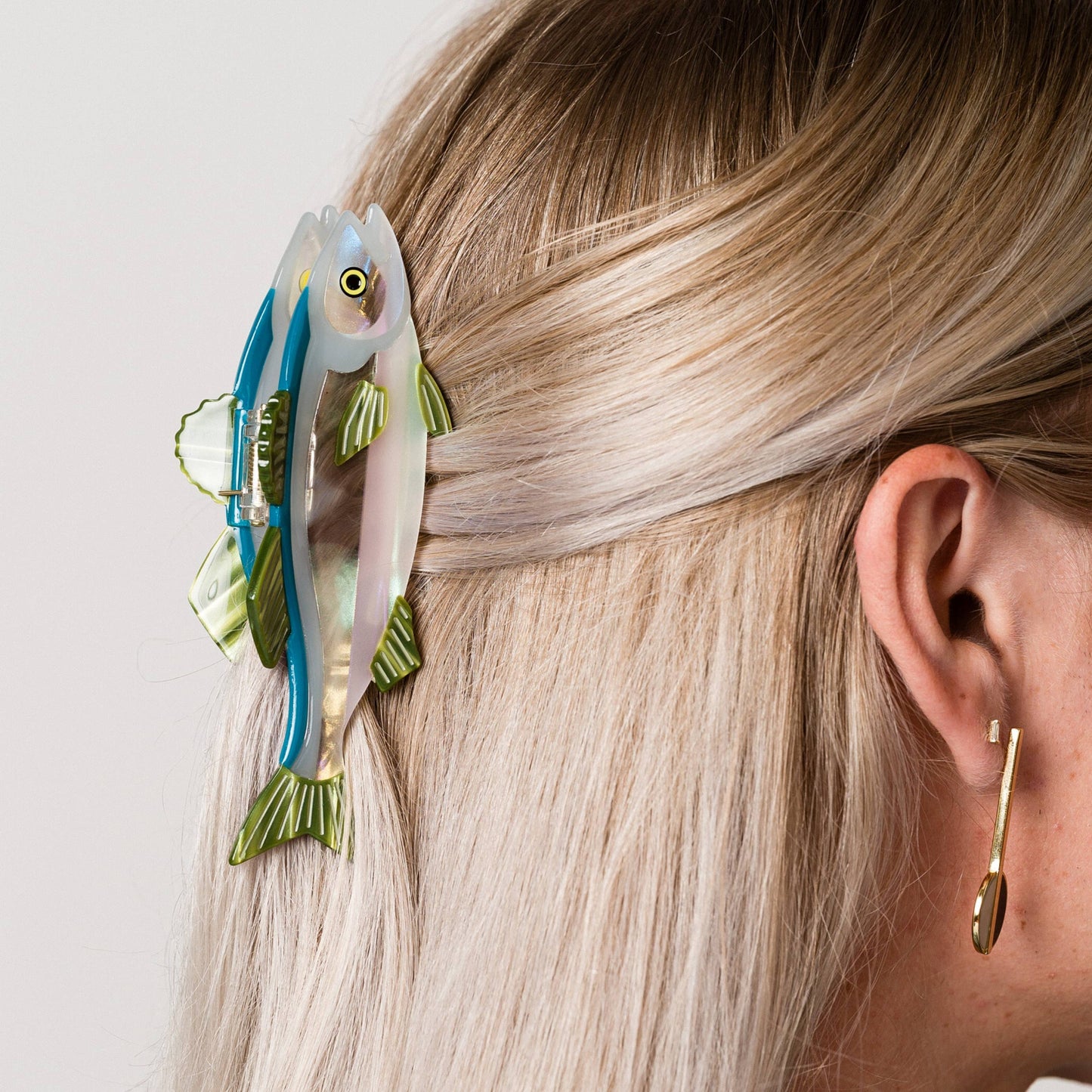 Person wearing a fish-shaped hair clip on light-colored hair with a neutral background