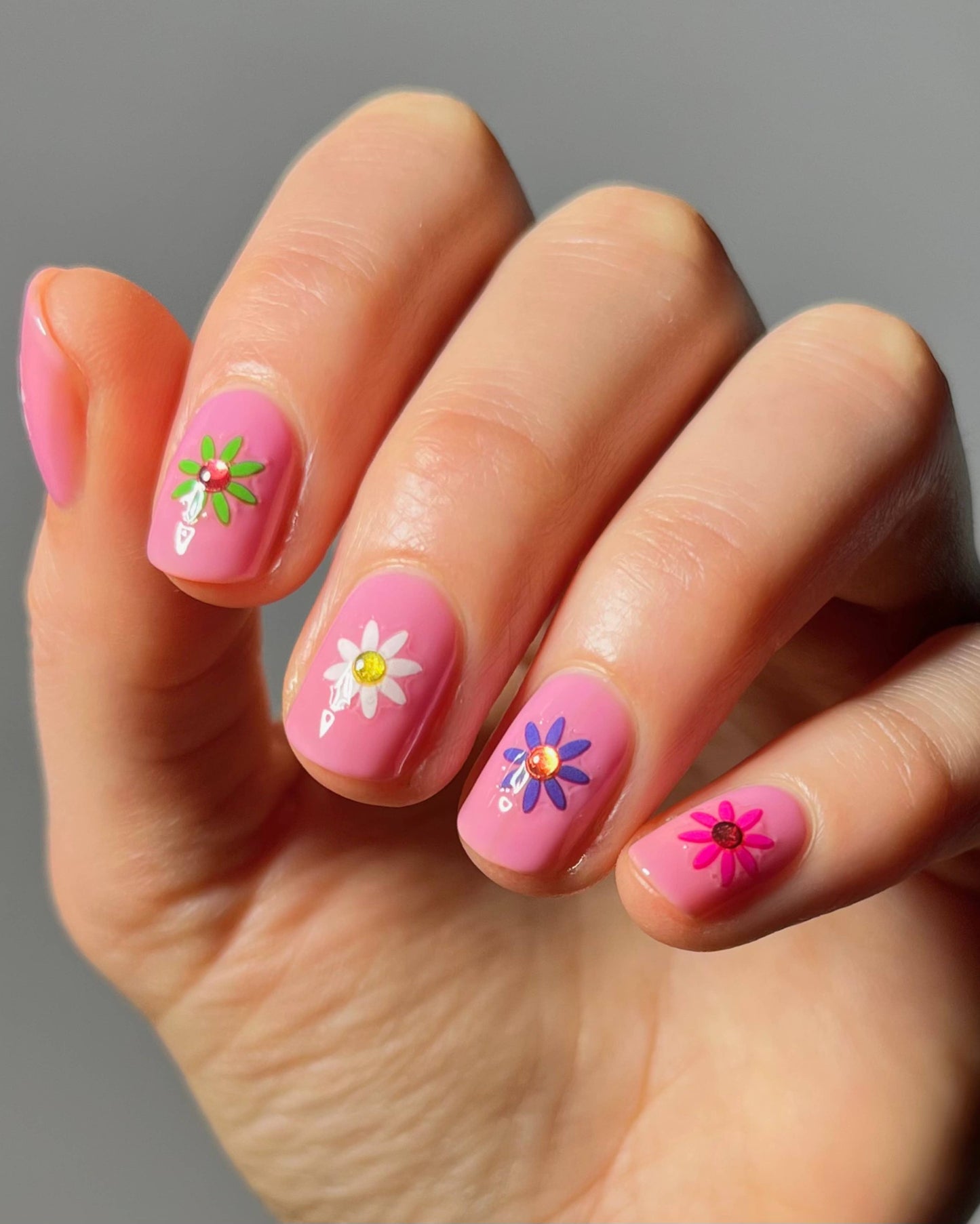Hand with pink nails featuring floral designs on a gray background