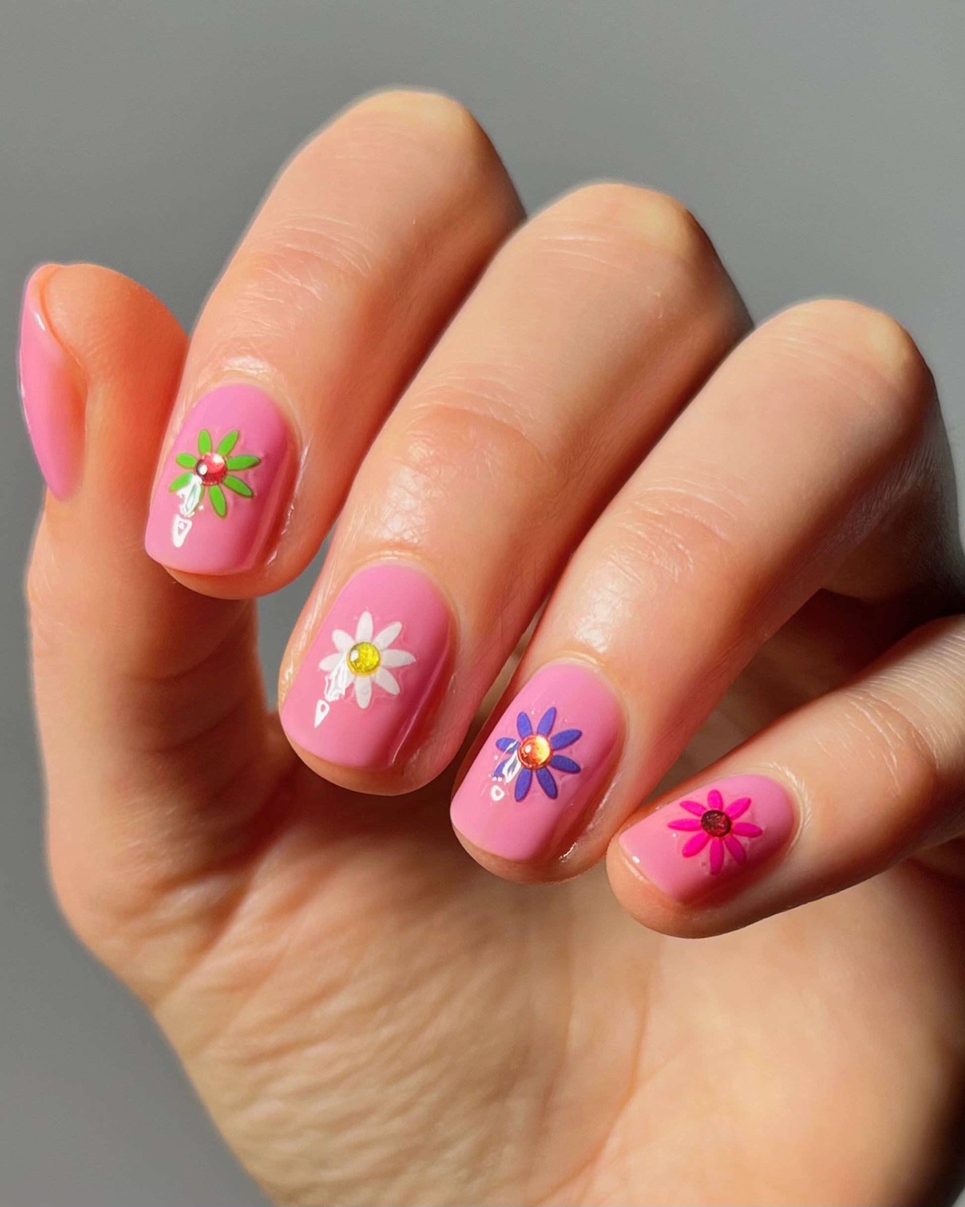 Hand with pink nails featuring floral designs on a gray background