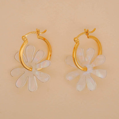 Gold hoop earrings with white floral designs on a beige background