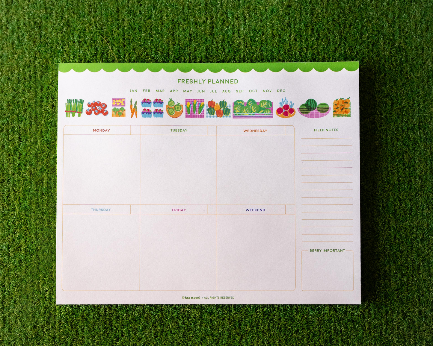 Weekly meal planner pad with colorful food icons on a green grass background