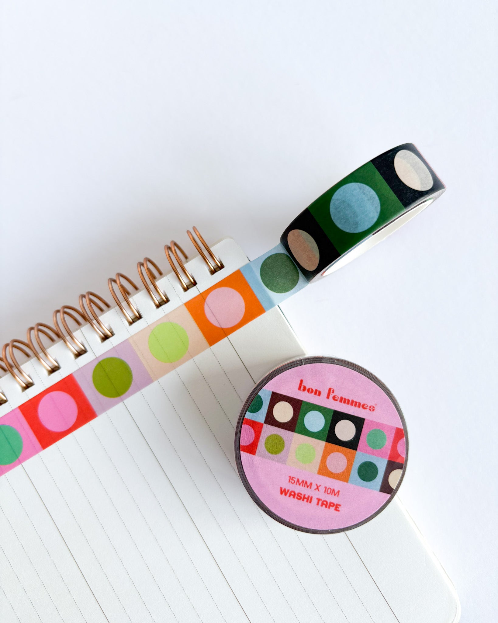 A roll of colorful washi tape with green, blue, pink, orange, and beige polka dots on a white lined notebook, alongside the round pink branded label of Fun Flemming Washi Tape.