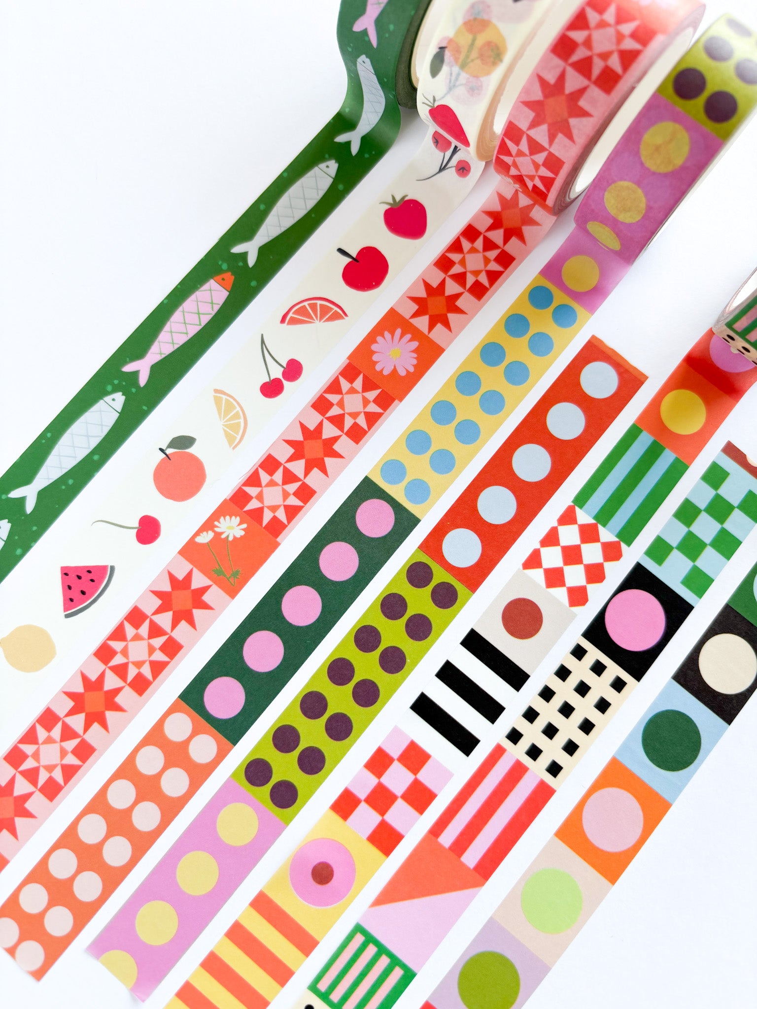 A set of colorful patterned washi tapes arranged diagonally on a white background, featuring various designs including fruit prints, geometric shapes, stripes, and polka dots.