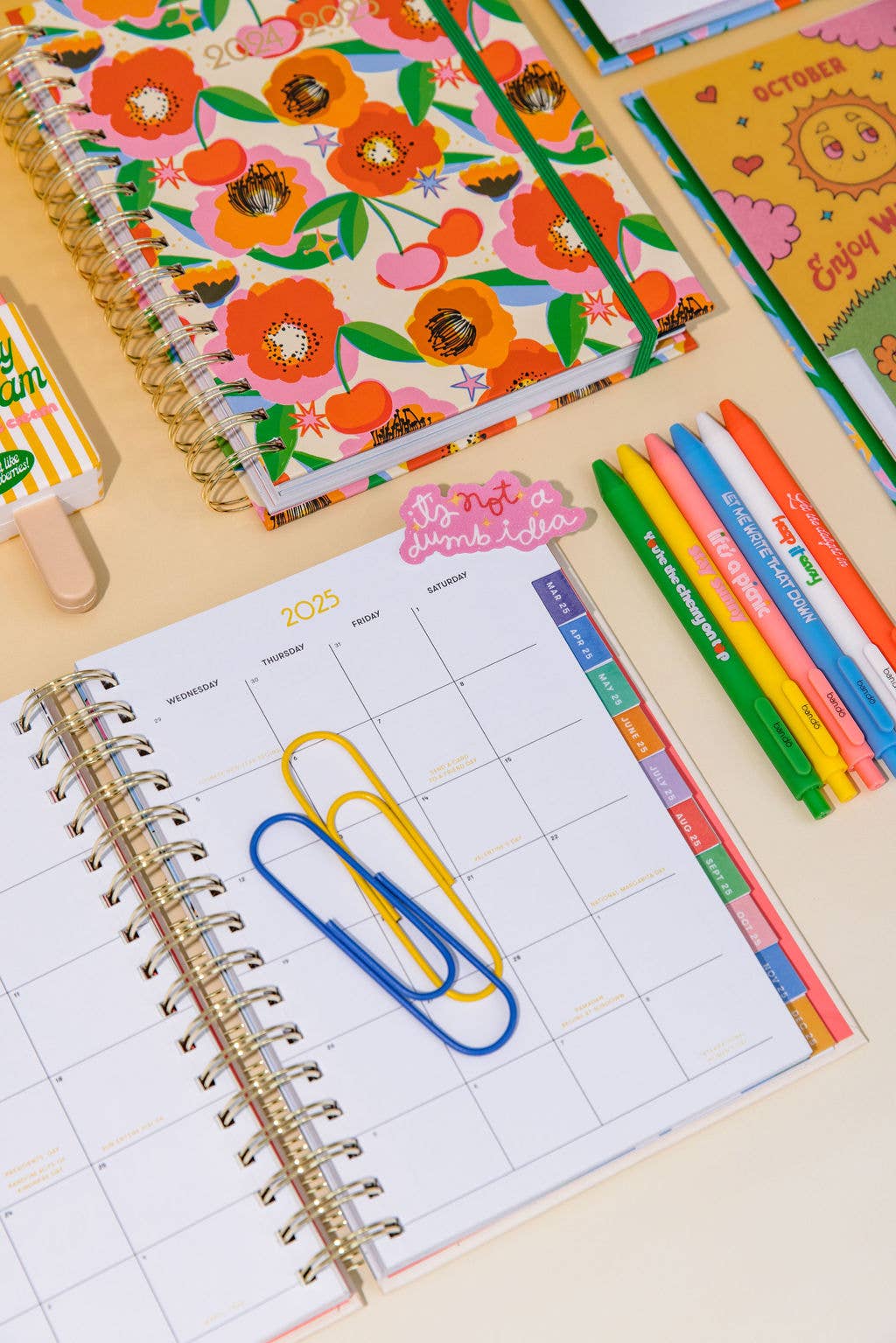 Open planner with colorful pages, markers, and a popsicle on a light background