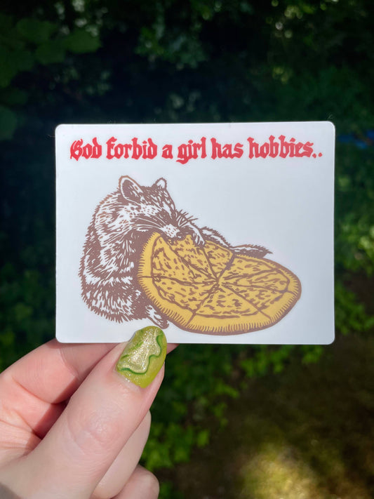 Card with a rat and pizza illustration and text held by a hand against a blurred green background