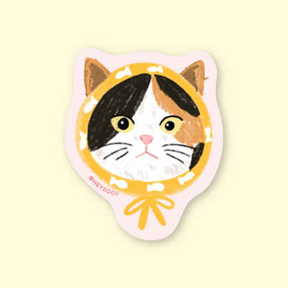 Sticker of a cat face with a yellow circle on a beige background