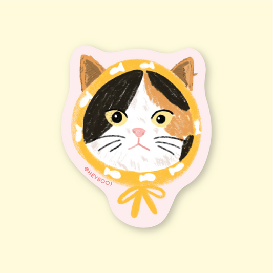 Sticker of a cat face with a yellow circle on a beige background