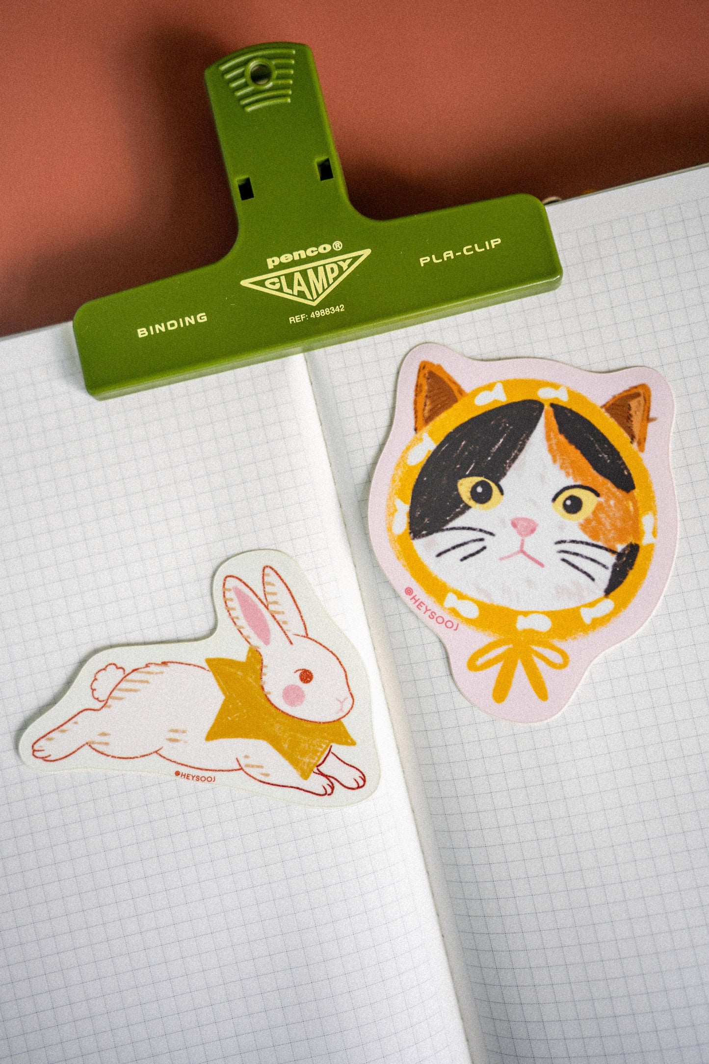 Two stickers, one of a rabbit and one of a cat, on a piece of paper with a green clip above them.