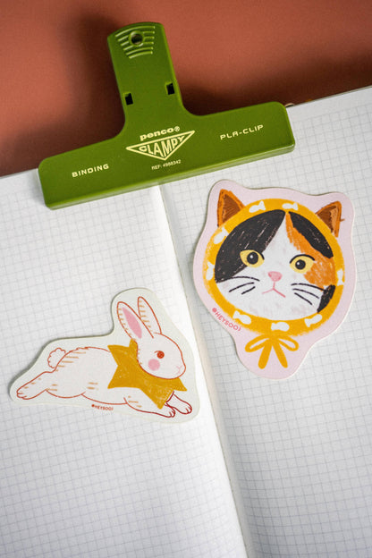 Two stickers, one of a rabbit and one of a cat, on a piece of paper with a green clip above them.
