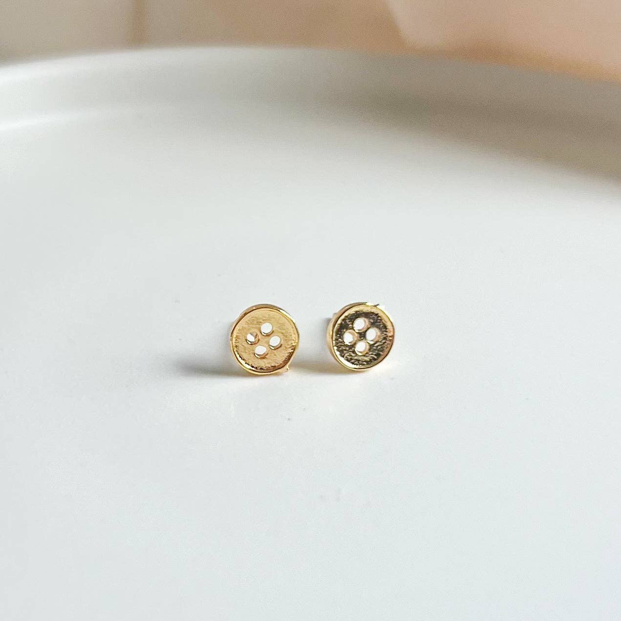 Gold button-shaped earrings on a light gray background