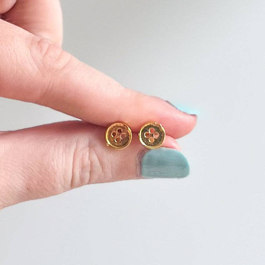 Gold earrings held between fingers against a neutral background