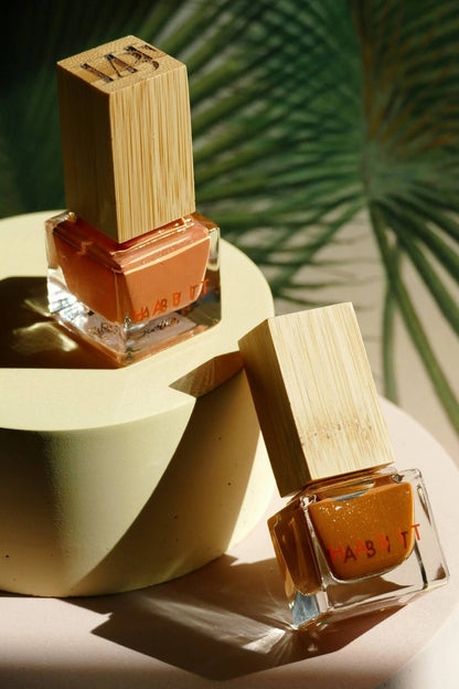 Two bottles of nail polish with a wooden cap on a light surface with a leafy background