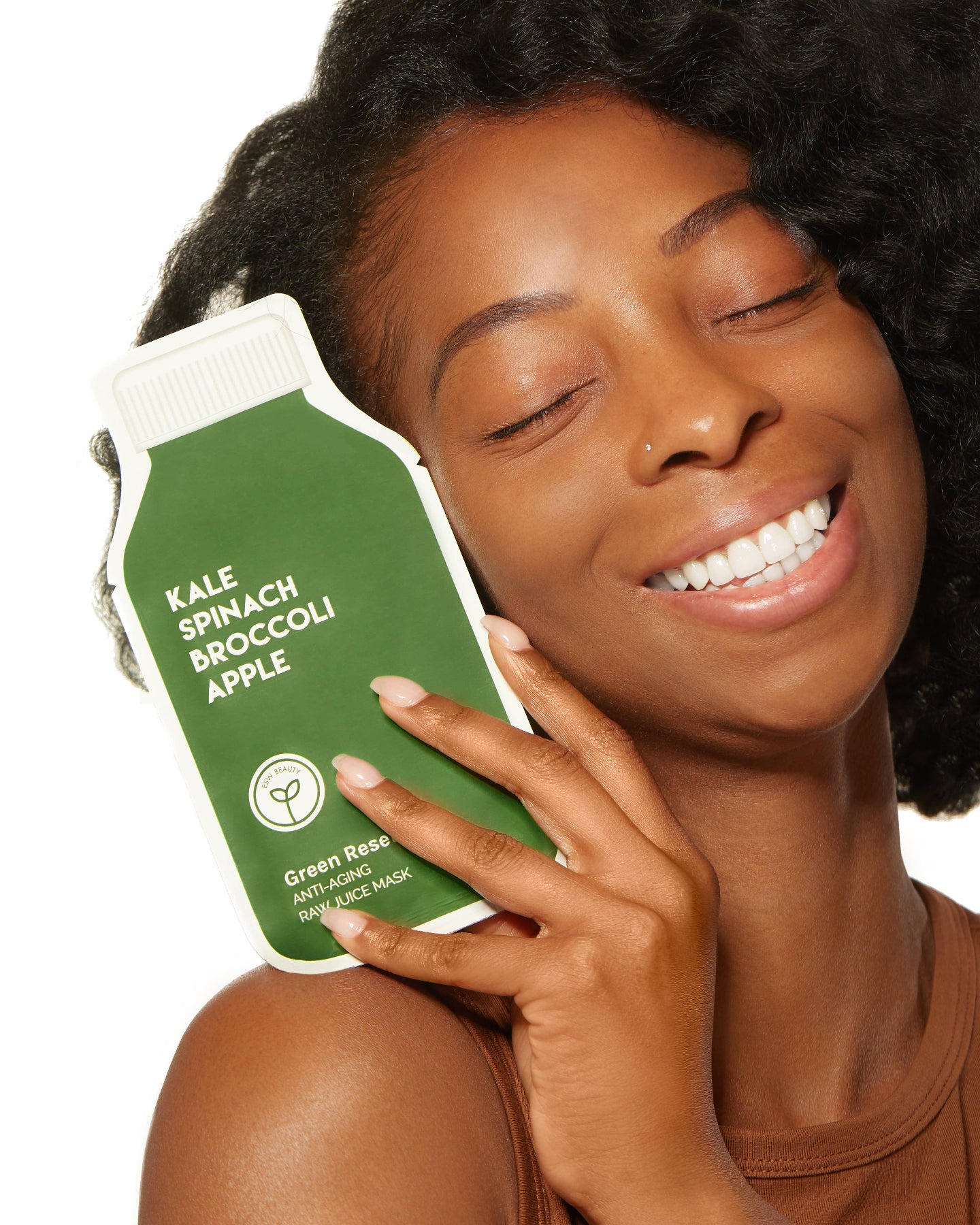 Woman holding a green skincare product labeled 'Kale Spinach Broccoli Apple' against a white background