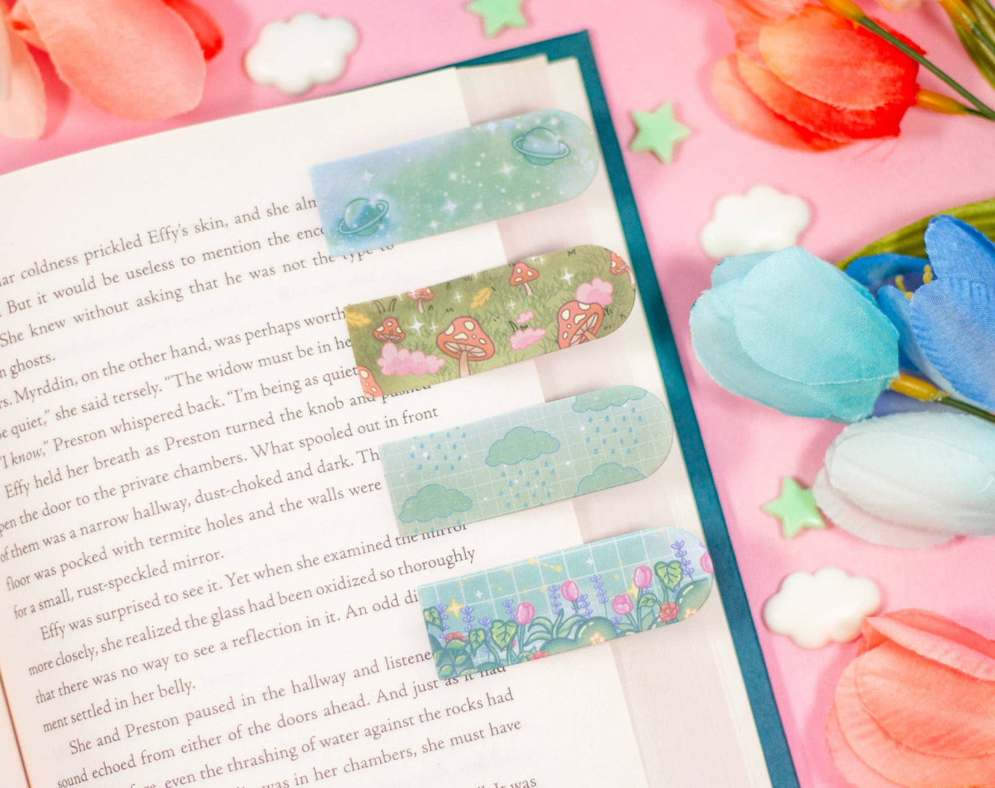 Decorative sticky bookmarks on a book with flowers and candies in the background