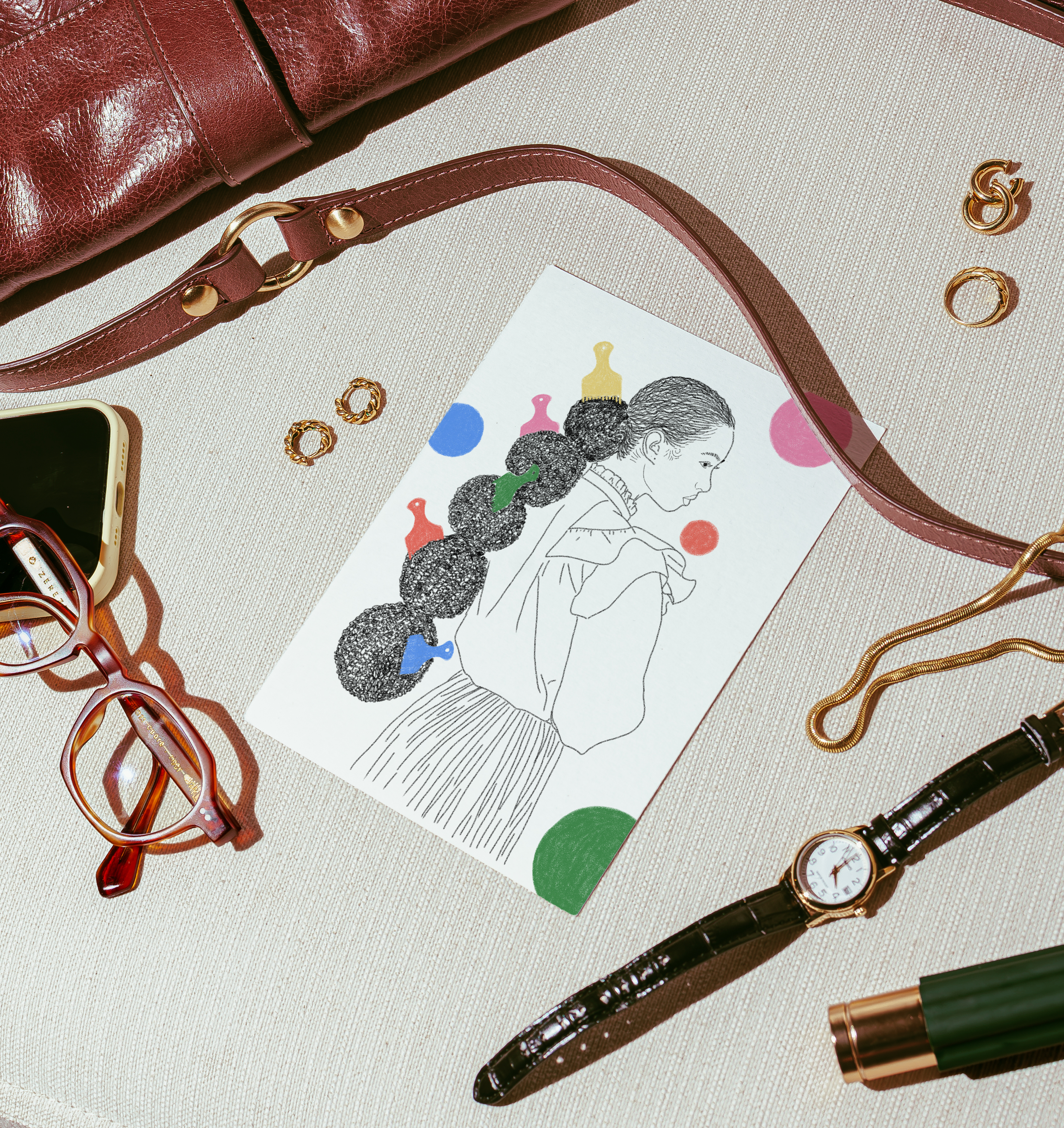 Flat lay of a watch, glasses, pen, and card with an illustration on a textured surface.