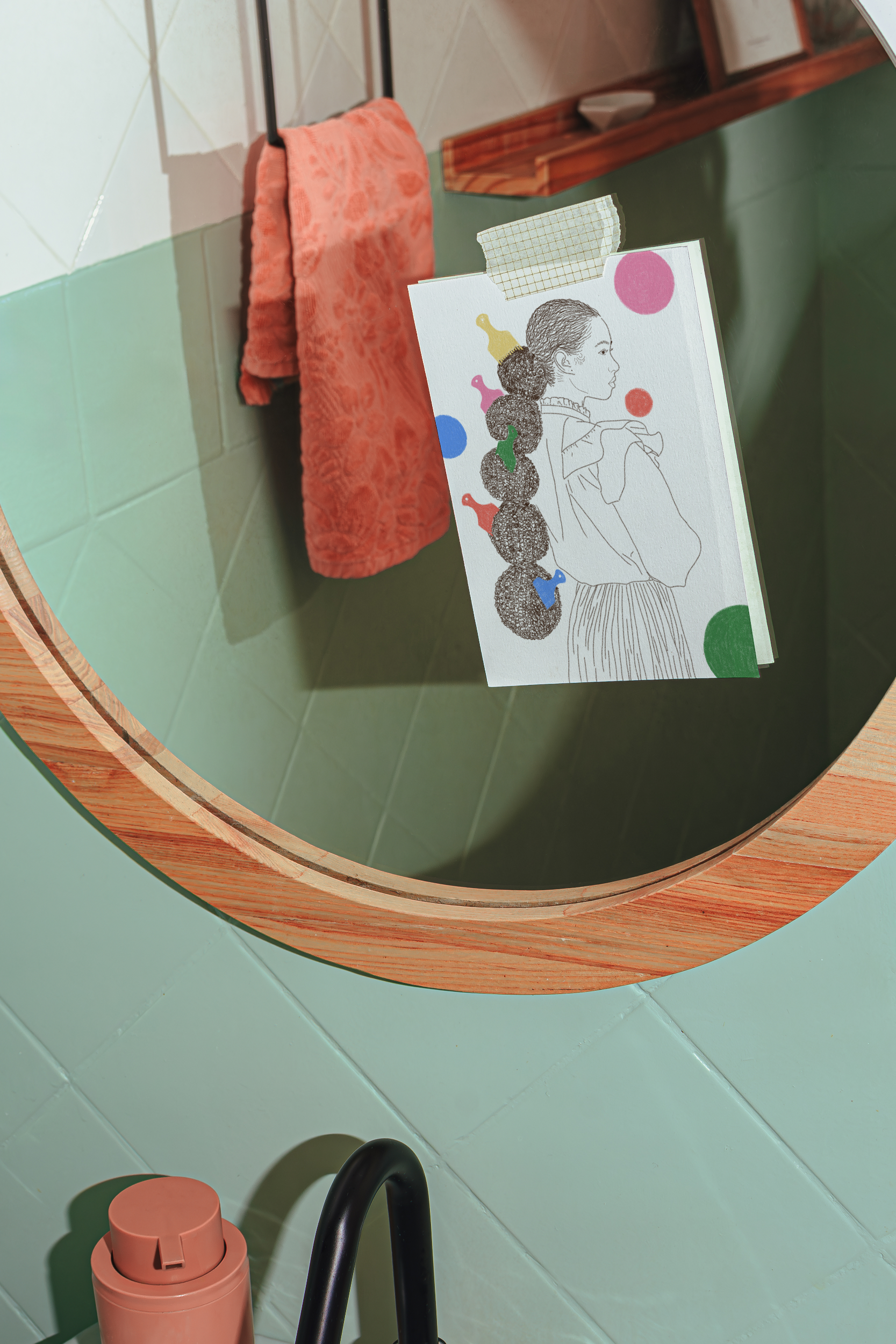 Round mirror with wooden frame on a light green wall, featuring a card with a colorful design.