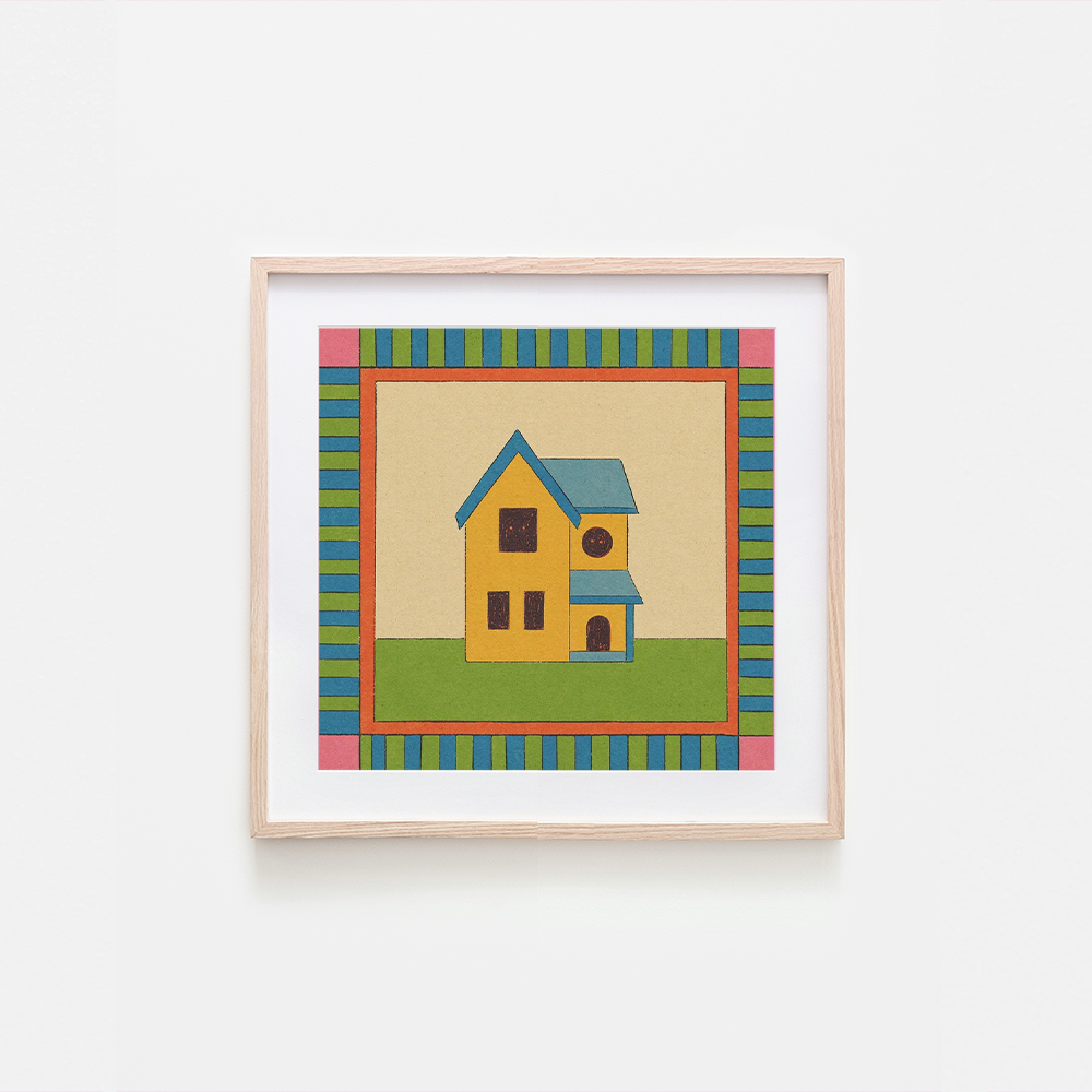 A framed art print featuring a whimsical yellow house with a blue roof, set against a beige background with a colorful striped border, hung on a plain white wall.