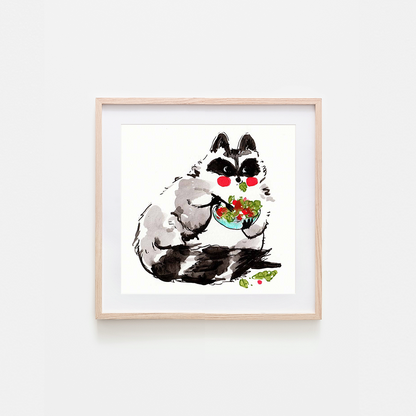 A framed art print featuring a whimsical watercolor illustration of a raccoon with black and white fur, red cheeks, and a bowl of salad, displayed on a light gray wall.