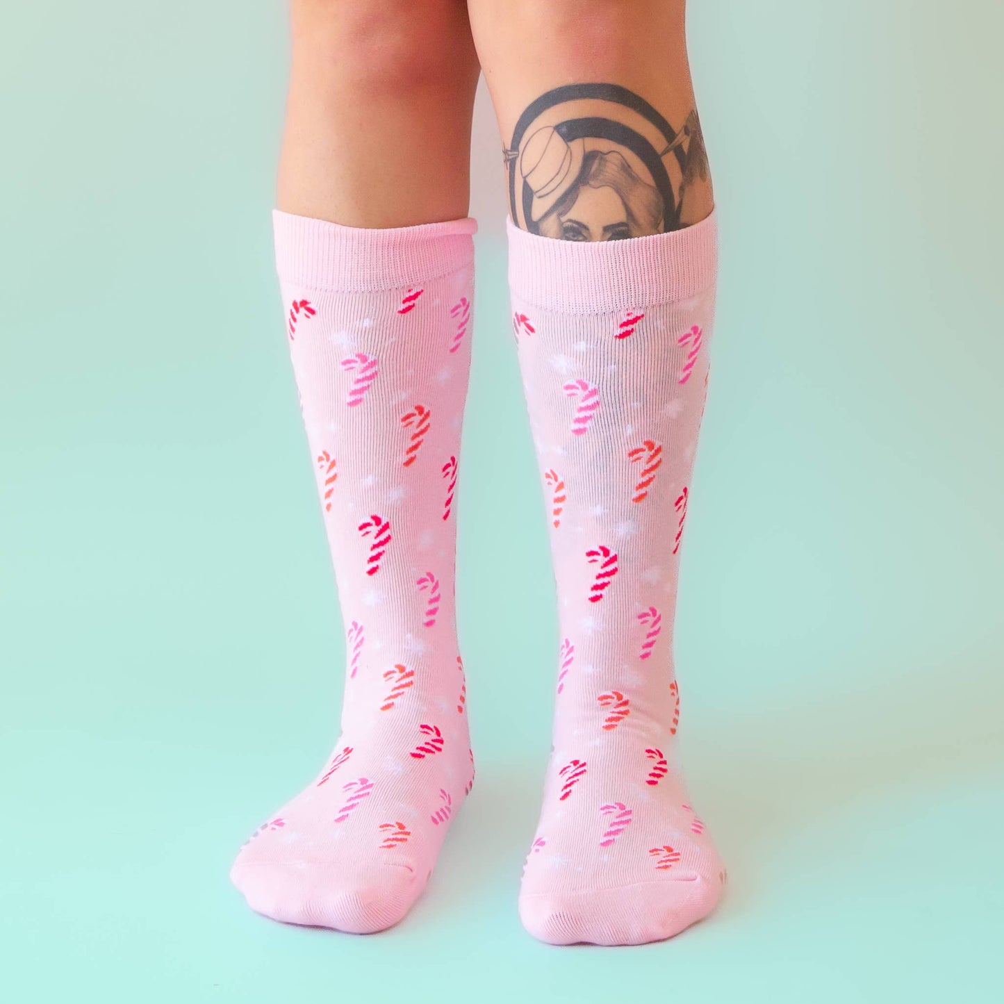 Pink knee-high socks with red and yellow patterns worn by a person on a light green background