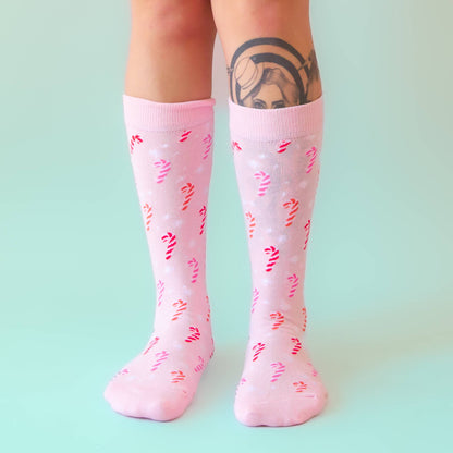 Pink knee-high socks with red and yellow patterns worn by a person on a light green background