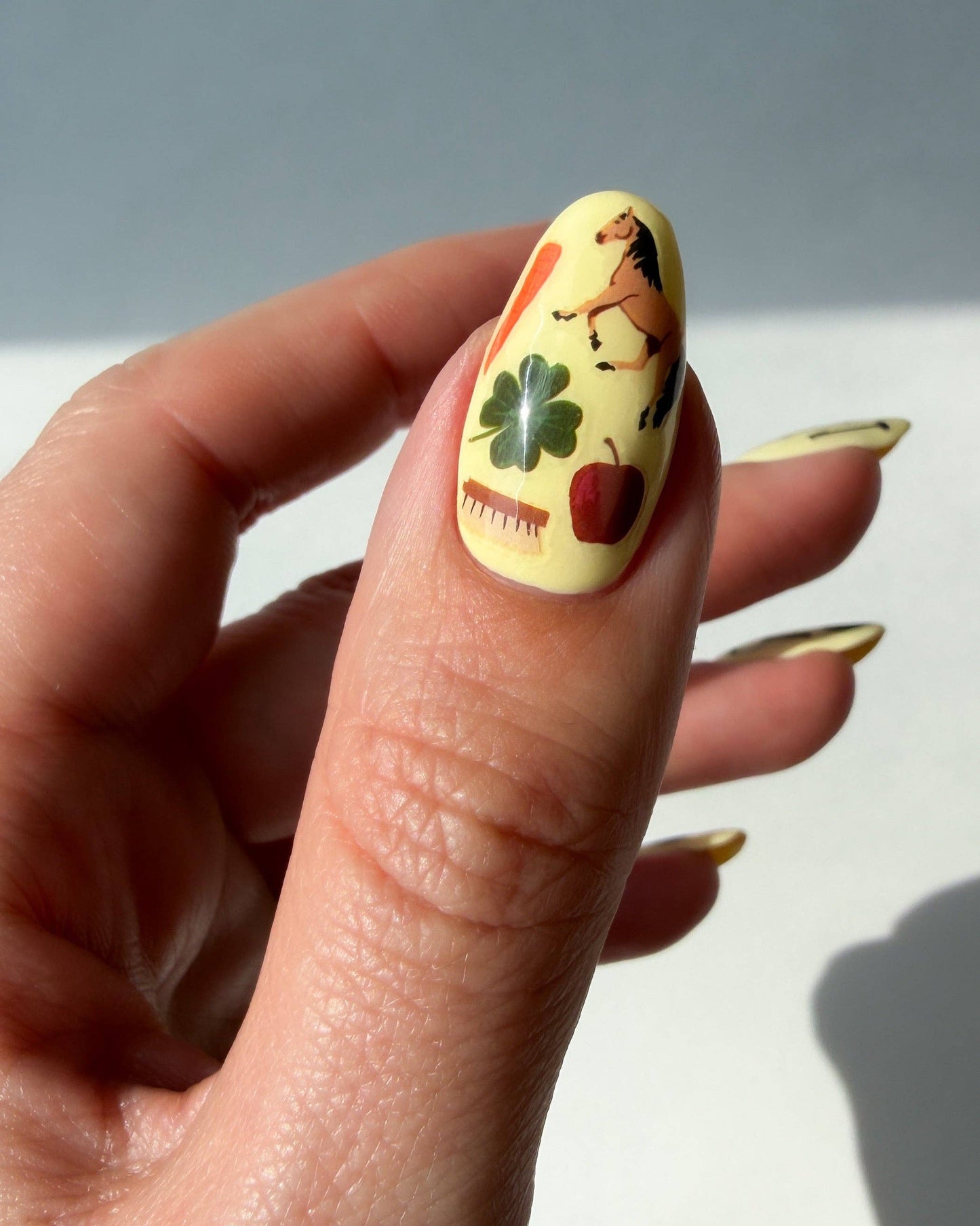 Nail with cartoon design of a horse, apple, and clover on a light background