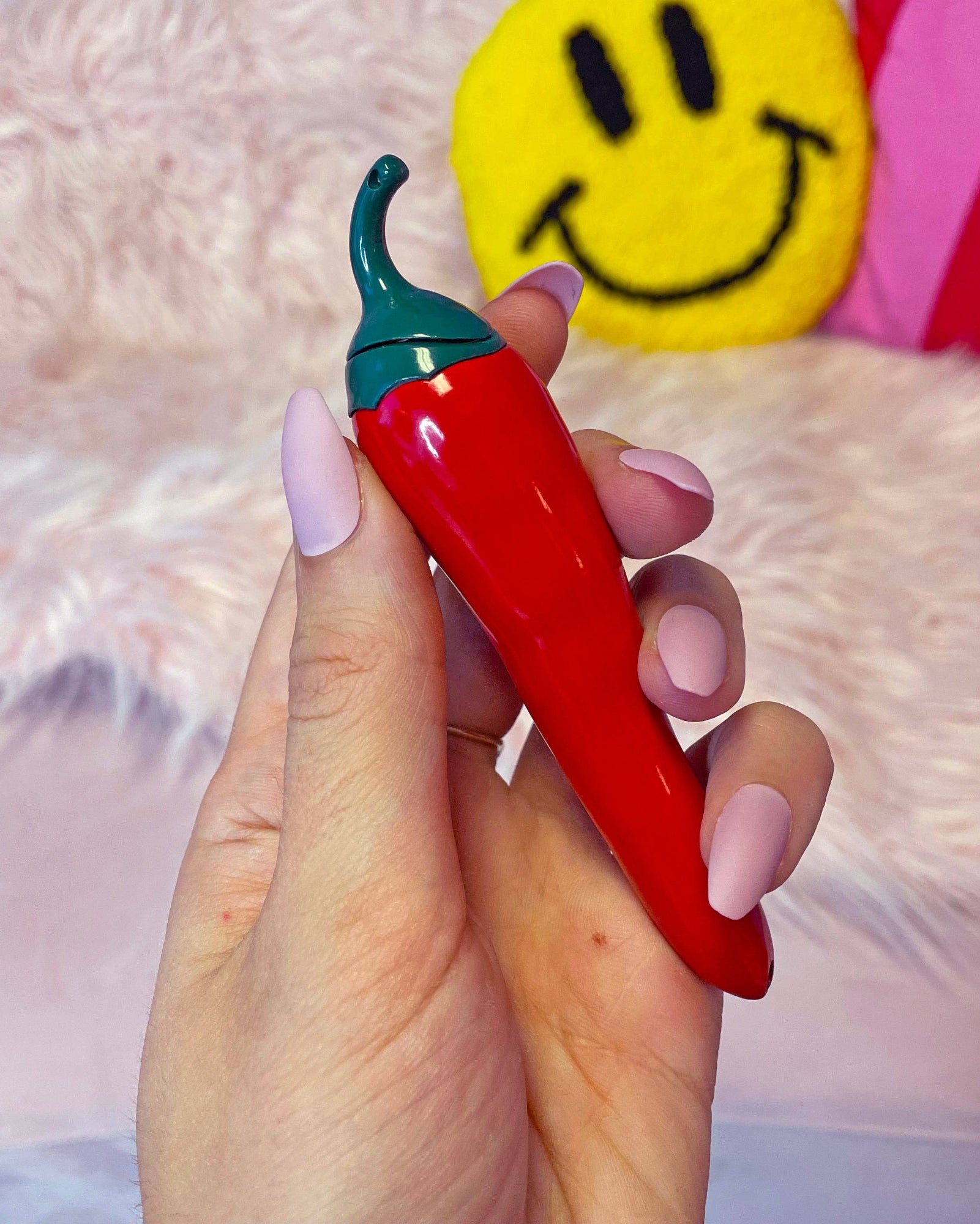 Hand holding a red chili pepper-shaped object with a green top against a soft pink background