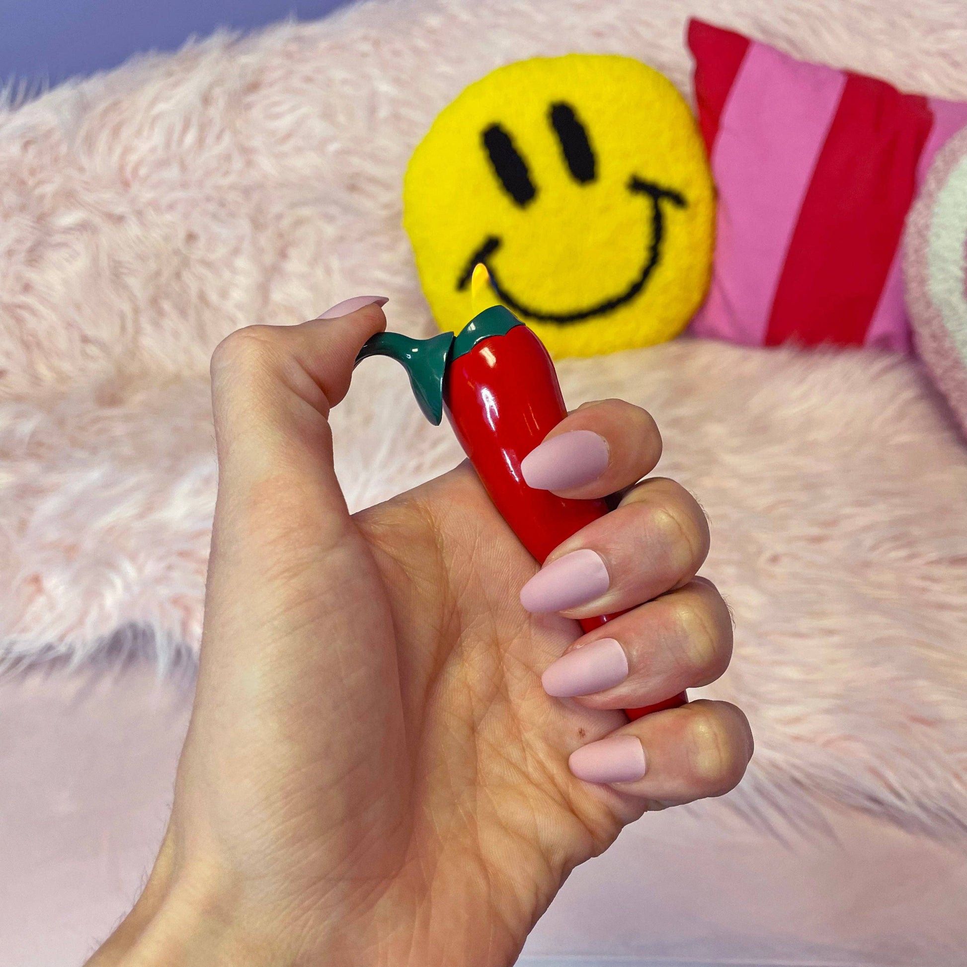 Hand holding a red toy with green stem against a colorful background