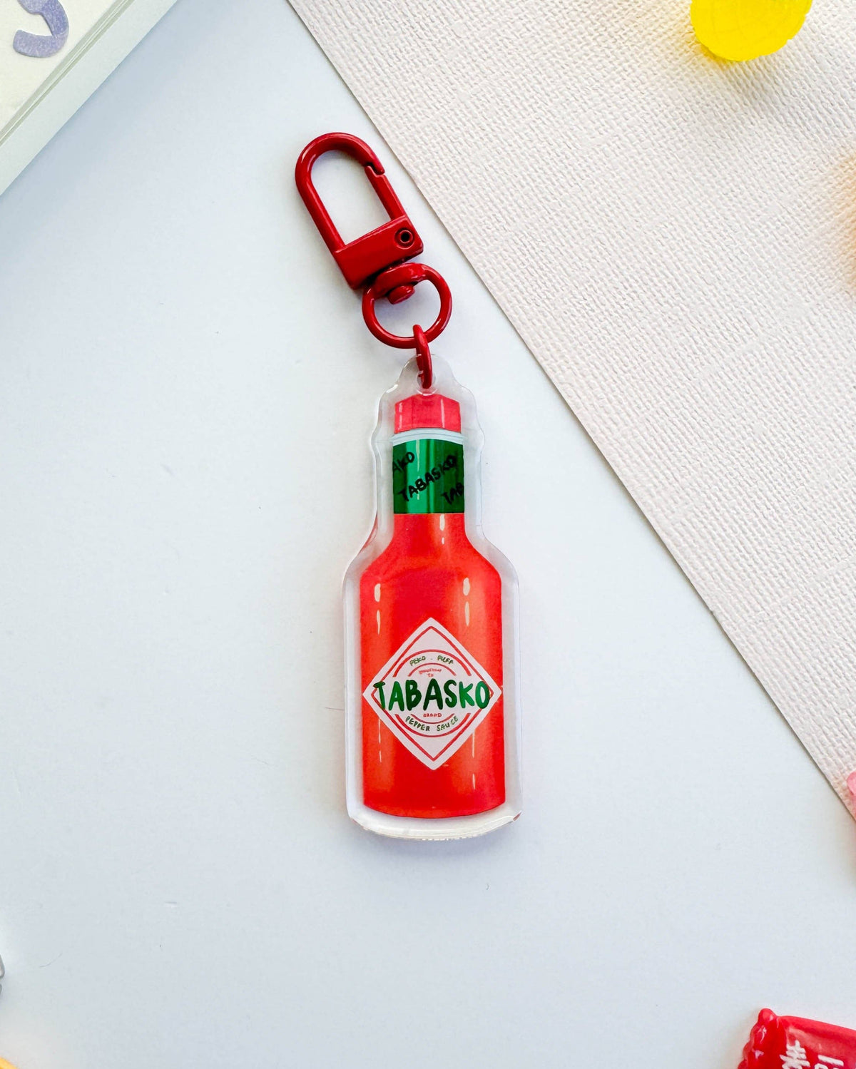 Tabasco sauce bottle keychain on a light blue surface with colorful items around