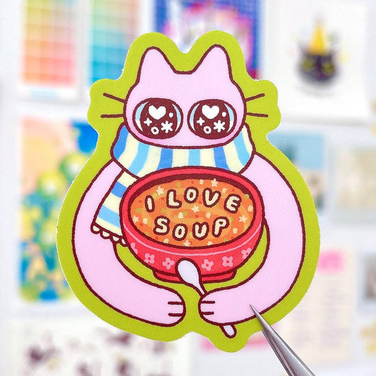 Cartoon cat holding a bowl of soup with 'I Love Soup' text, surrounded by colorful blurred items.