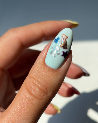 Nail with light blue polish, star, and bear design held by a hand against a blurred background