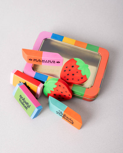 Colorful strawberry-shaped erasers in a tin box on a light gray background