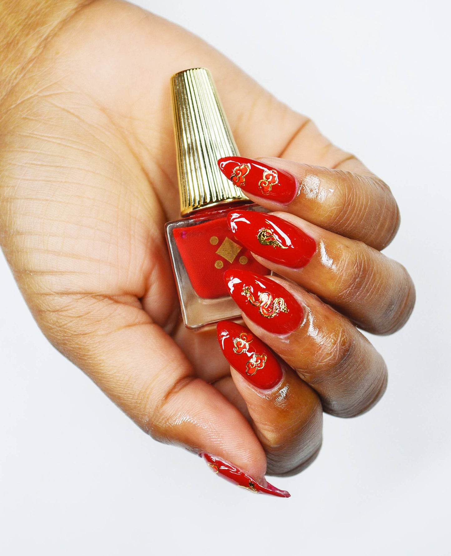 Hand with red nail polish holding a bottle of red nail polish.