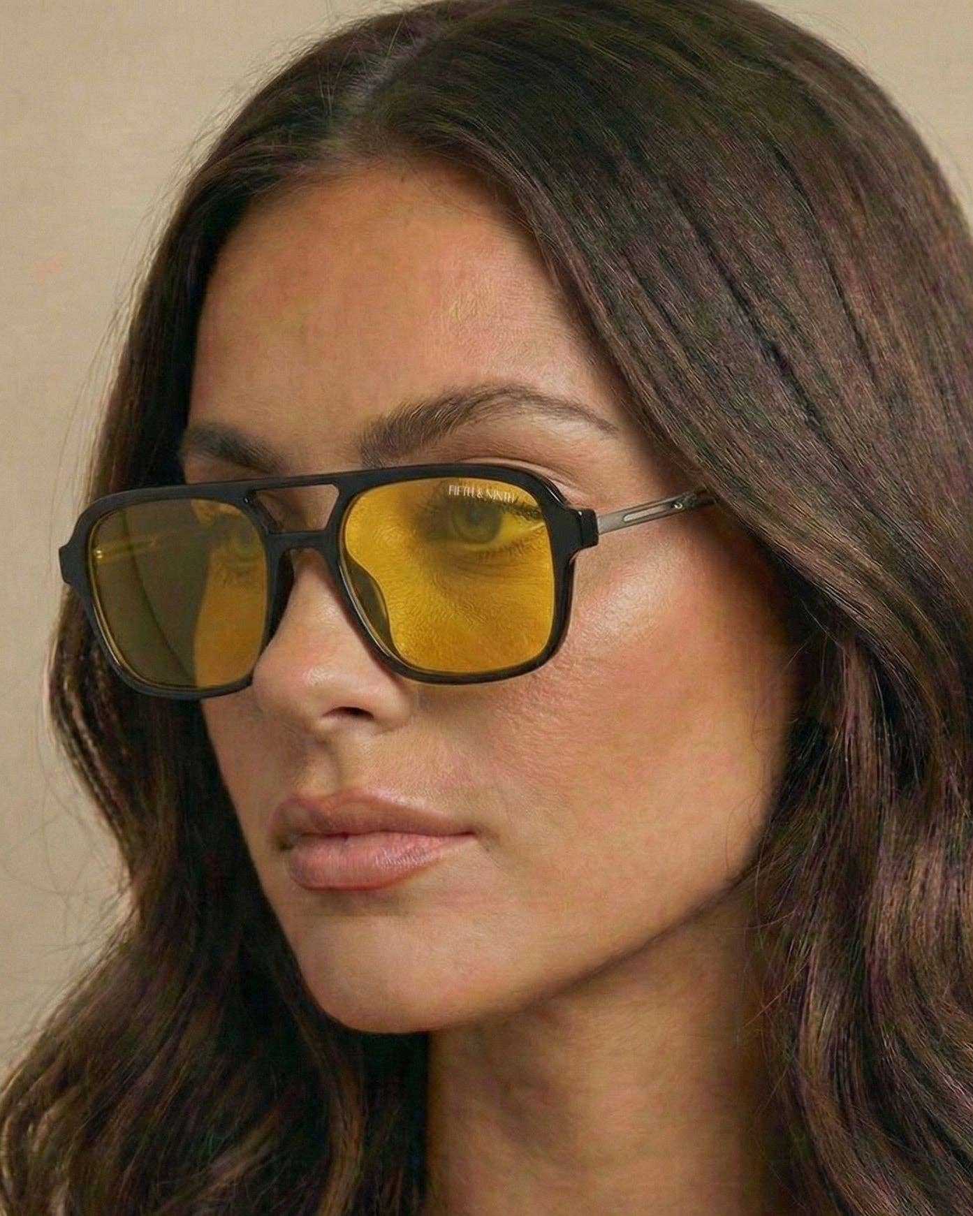 Woman wearing sunglasses with yellow lenses against a neutral background