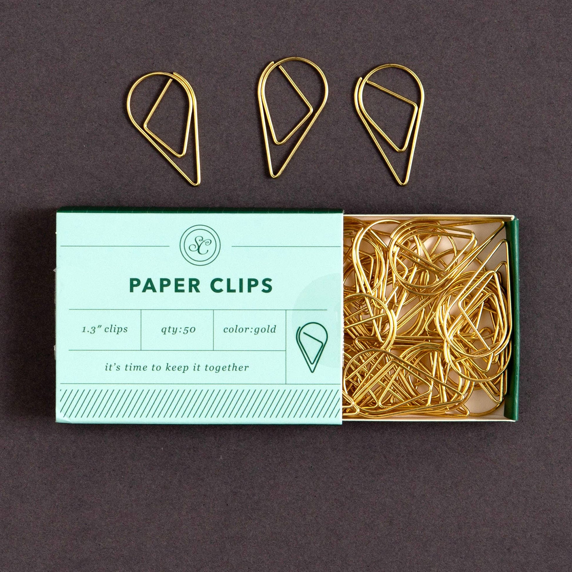 Gold paper clips on a box labeled 'Paper Clips' with a dark background
