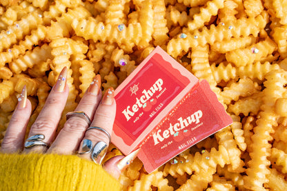 Hand holding a packet of Ketchup themed nail files with fries in the background