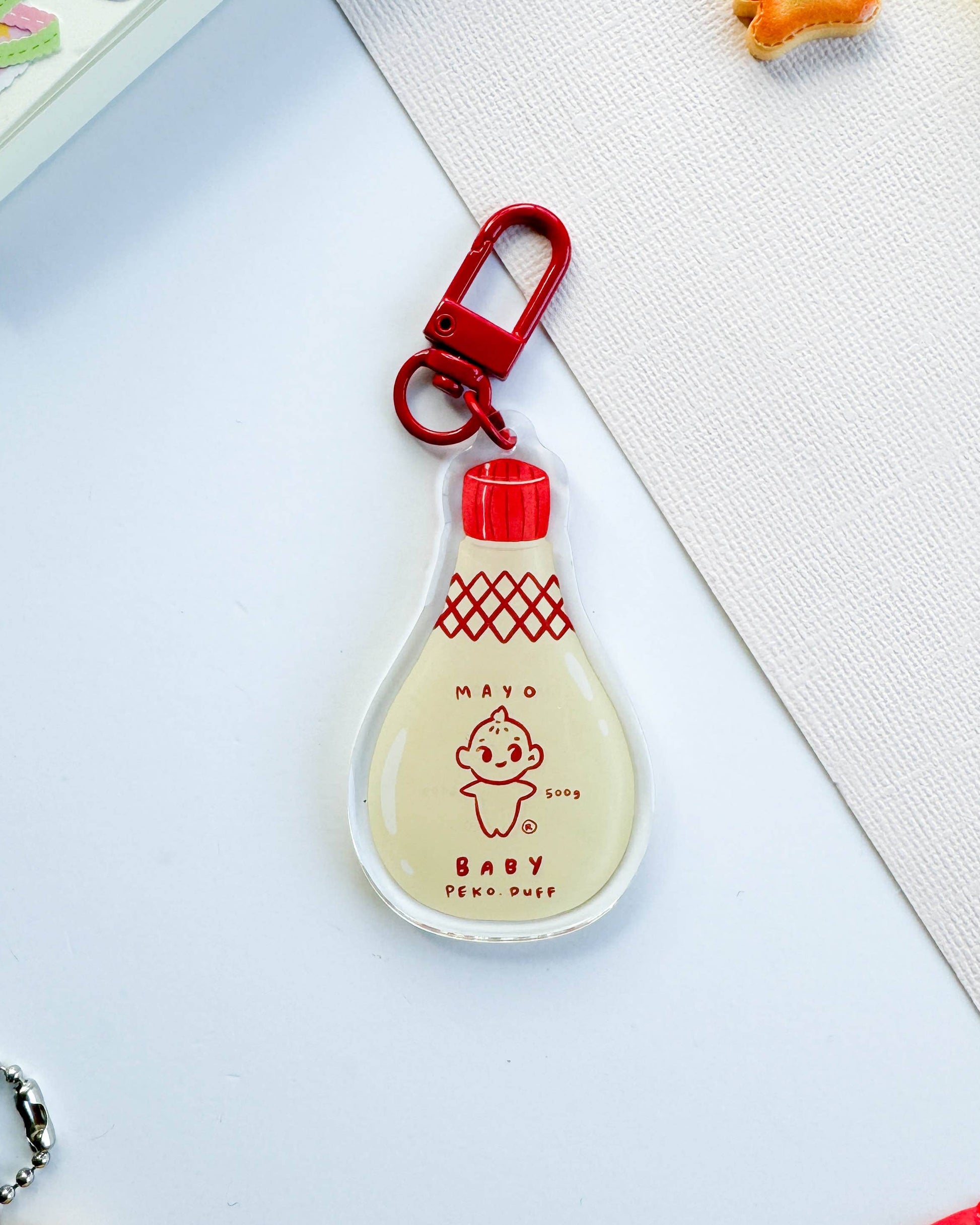 Keychain shaped like a bottle with a red cap on a light gray surface 