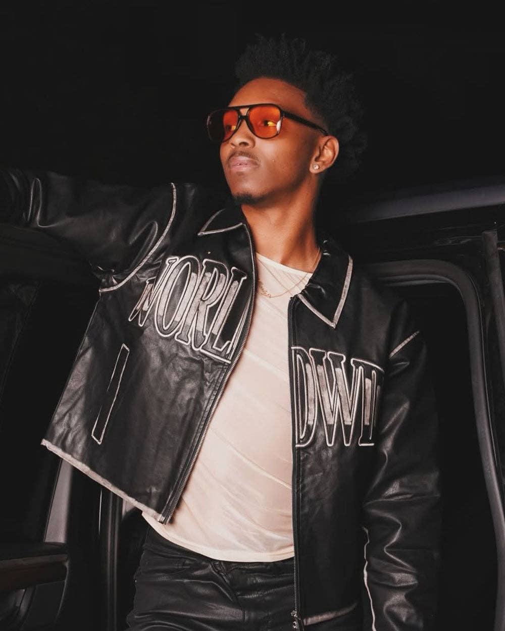 Person wearing a black leather jacket with standing next to a car at night.