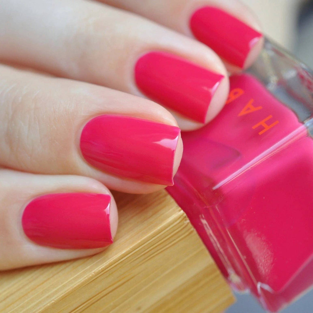 Hand with pink nail polish holding a pink nail polish bottle.