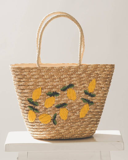 Woven bag with lemon designs on a white stool against a light gray background