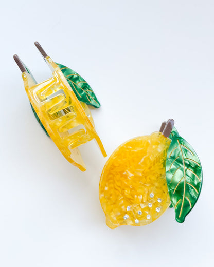 Yellow lemon-shaped hair clips with green leaves on a white background
