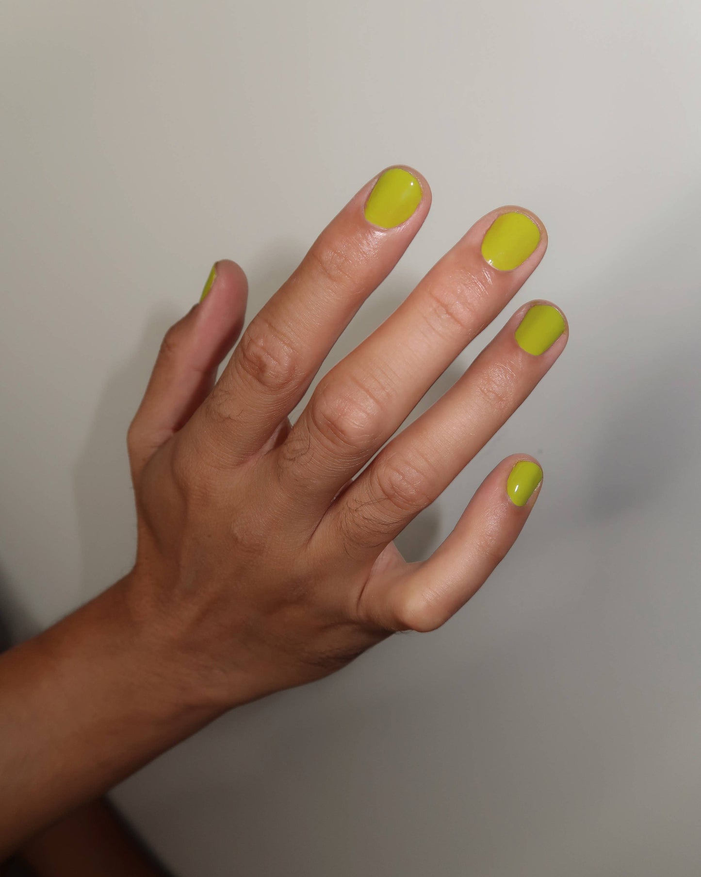 Hand with neon green nail polish on a plain background, Lily Chartreuse Nail Polish Ruth Polish