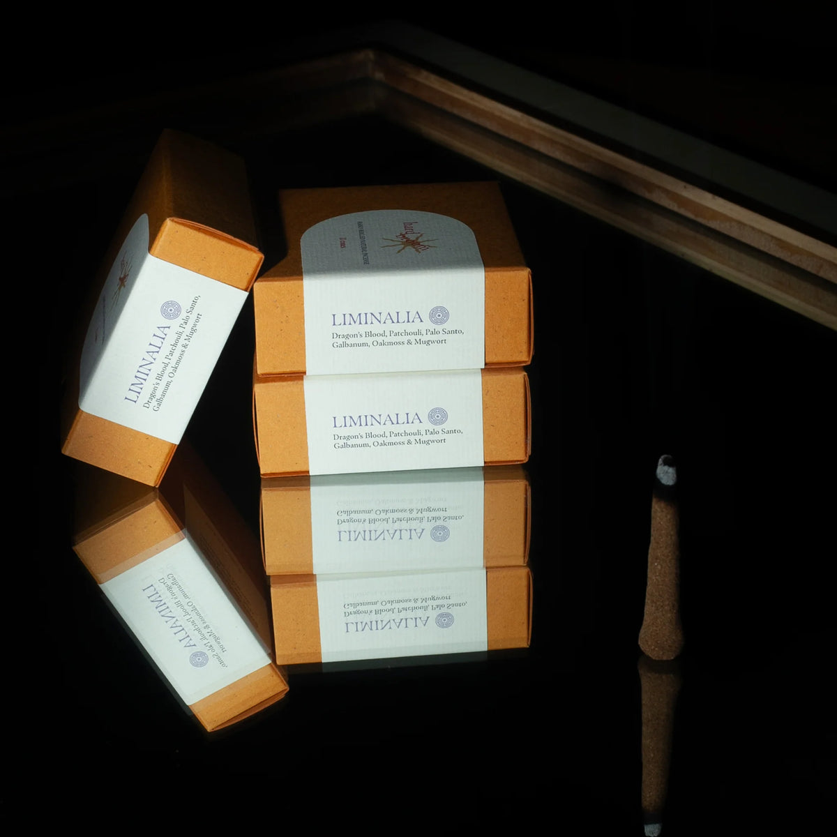 Three orange and white Liminalia boxes arranged on a glossy black reflective surface, with a wooden tray edge visible in the background.
