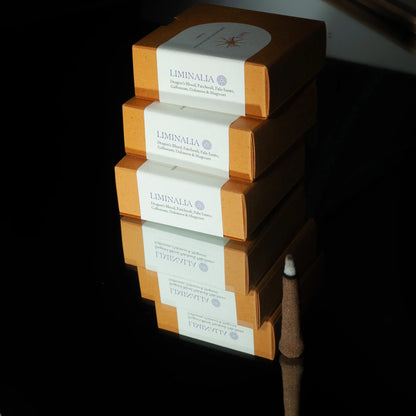 Three stacked Liminalia incense boxes in warm orange-brown packaging with white paper bands, photographed on a glossy black reflective surface.