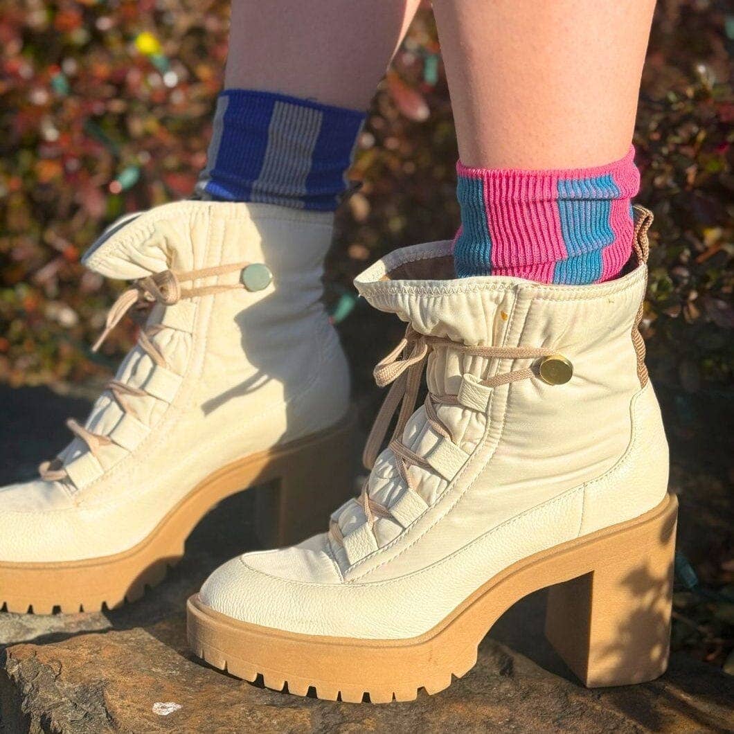A pair of off-white lace-up ankle boots with chunky tan platform soles, worn with pink and blue striped socks outdoors on stone steps.