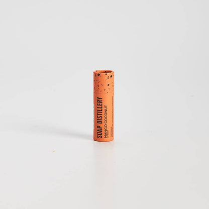 Cylindrical container with cork-like texture and 'SOAP DISTILLERY' branding on a white background. Mango Coconut Lip Balm