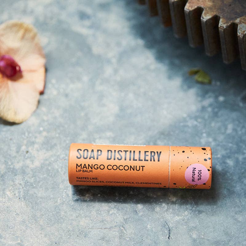 Soap Distillery Mango Coconut lip balm on a textured surface with natural elements.