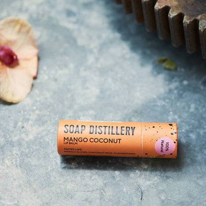 Soap Distillery Mango Coconut lip balm on a textured surface with natural elements.