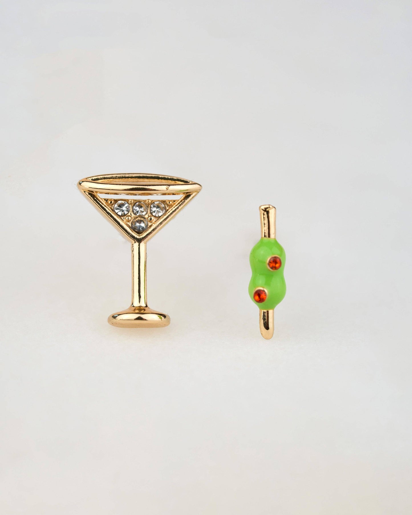 Gold martini glass and olive-shaped earring on a light gray background